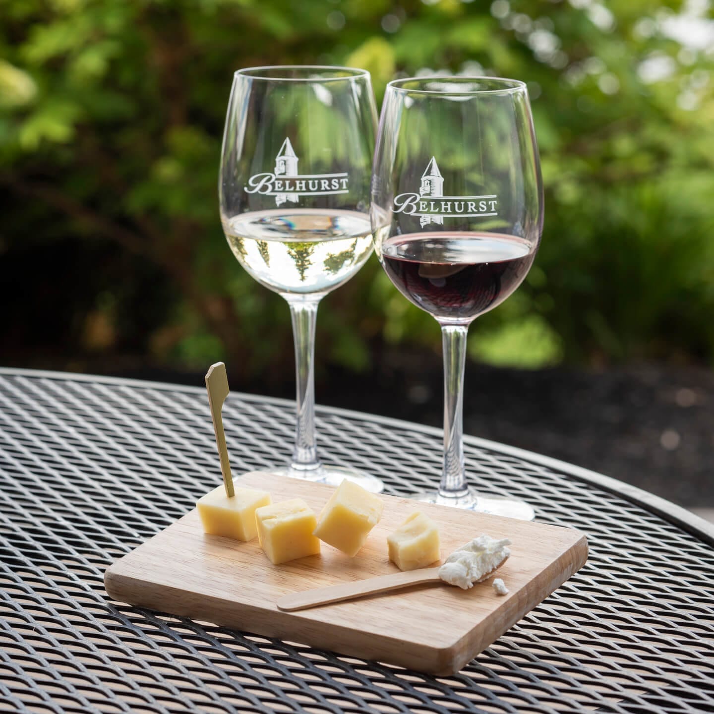 Two wine glasses and wooden tray of cheese on a patio table.