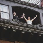 Lina and Matt opening champagne out a window.