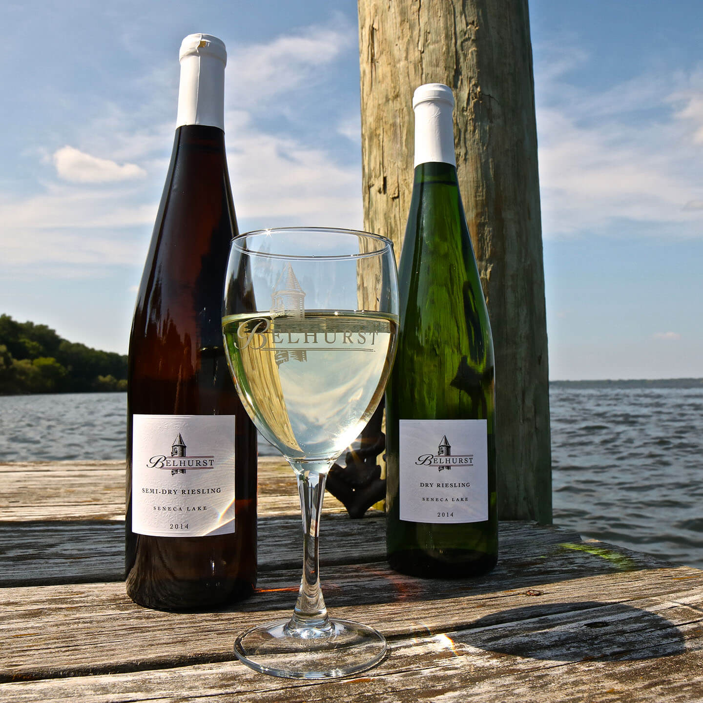 Two wine bottles and a glass of white win sitting on a dock.