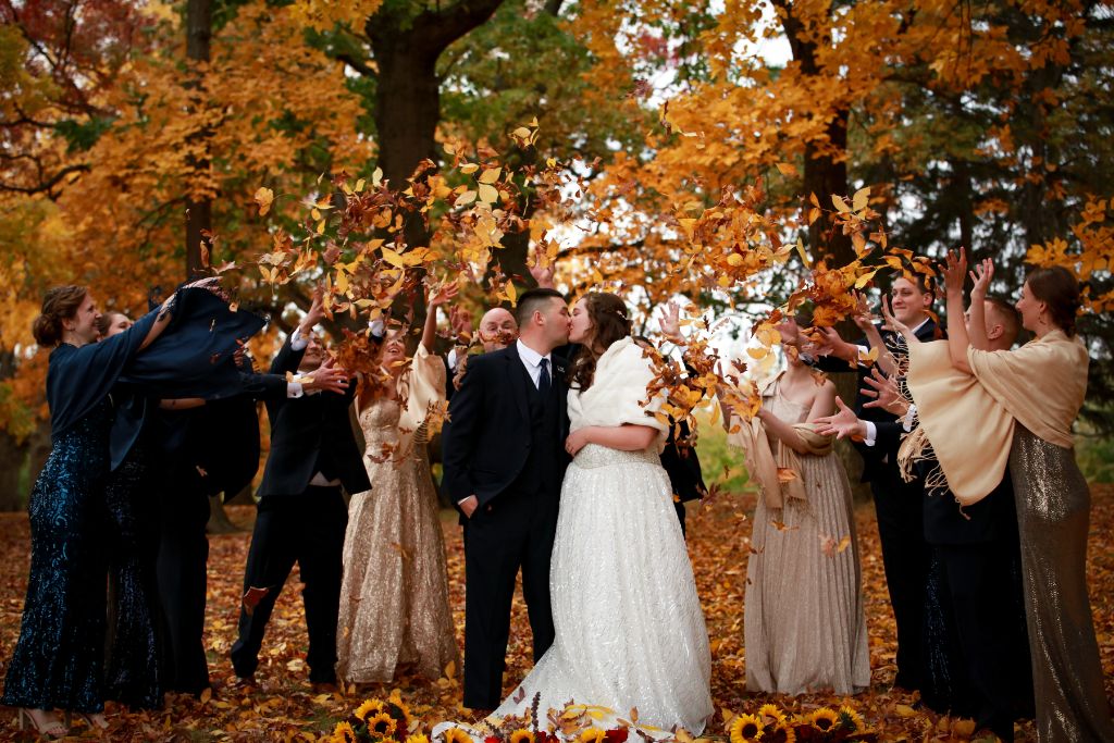 Bride and Groom kissing in Autumn. Wedding party throwing leaves. Photo by Tellier studios